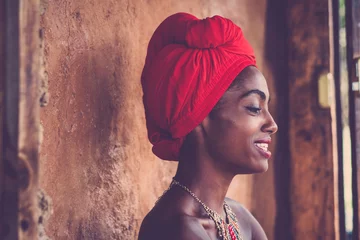 Traditionelles Mädchen der afrikanischen Schönheit, das lächelt und schaut - schönes Porträt für hübsche Frau mit schwarzer Haut - traditionelles Kleid und nackte Haut - attraktives Afrodamengesicht mit ländlicher Wand im Hintergrund © simona