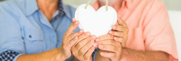 Valentine's day concept couple man and woman old senior taking white wooden heart together -...