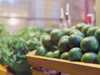 Mint and lime for making a cocktail are in wooden boxes on the counter of a street cafe. In the background are bottles of syrup or alcohol.