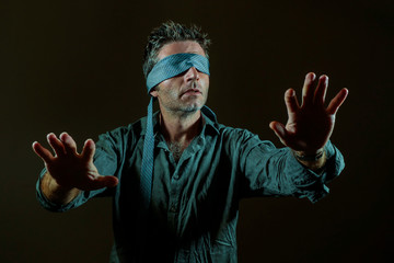 young lost and confused man blindfolded with necktie playing internet trend dangerous viral challenge with eyes blind isolated on black background