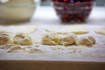 flour, dough and cherries lying on the table, the process of preparing buns and pies