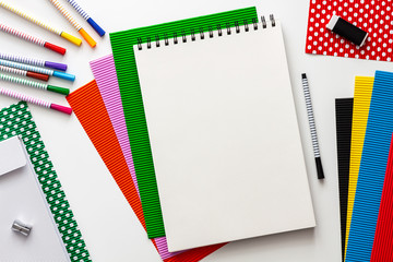 Creative school desk with sketchbook mockup. Colorful school supplies. Papers and markers. Place for text. View from above