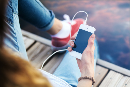 Young woman sitting on pier holding a smartphone