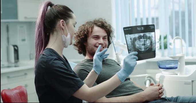 Happy patient at dentist have a friendly conversation with his doctor , the dentist shows to the patient his results of teeth X-ray , they both are smiling in dentist room. shot on red epic