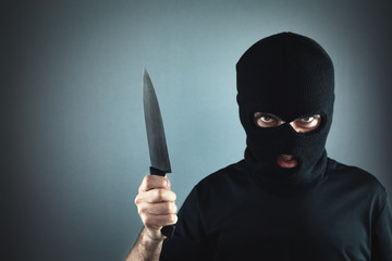 Killer in black mask threatening with knife. Crime and robbery concept