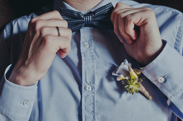 Groom in a shirt with a bow tie and a boutonniere. Flower design, floristry. Wedding day and accessories