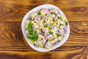 Tasty salad with sausage, green pea, canned corn, bell pepper, cucumber and mayonnaise on wooden table. Top view