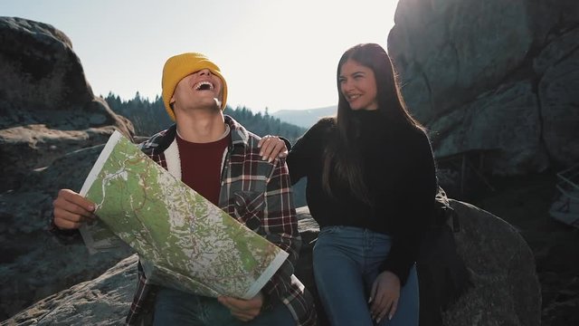 Travel to the mountains. Beautiful couple in love sits on the rock and learns a map. They talk with each other, laughing and having fun