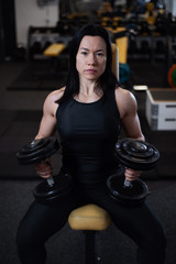 fitness girl trains with dumbbells in the gym. Resting between sets