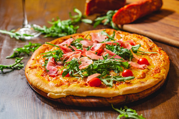 Italian pizza with prosciutto (parma ham), arugula (salad rocket) and cherry tomatoes on wooden board. Close up