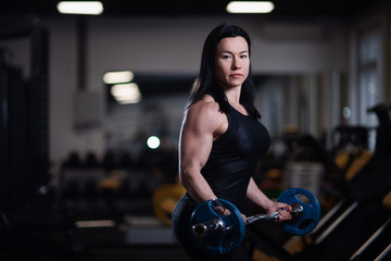 Fototapeta na wymiar fitness girl trains biceps with barbell in the gym.