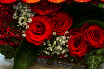 Bouquet of red roses with white gypsophila and artificial red berries, with ivy leaves and other large leaves in a decorative box



