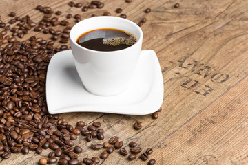 Eine Tasse mit frisch gebrühtem Kaffee und Kaffeebohnen auf einer Holzoberfläche