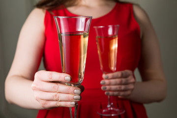 Valentines day romance, beautiful woman in red dress holding champagne glasses in hands,close up.