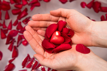 Valentines day surprise, close up woman holding red rose petals and hear candle in hands