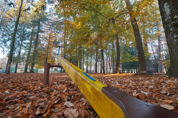 Old yellow seesaw in park viewed from the ground looking up.  Shot in autumn with leaves coverage, and colorful trees. Wide angle capture from bottom