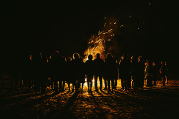 silhouettes of people standing  around large bonfire with sparks flying around - Powered by Adobe