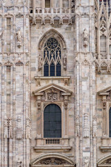 Fototapeta na wymiar Vertical: Duomo di Milano exterior architectural details with statues, sculpture, bronze door, window, stonework, and facade