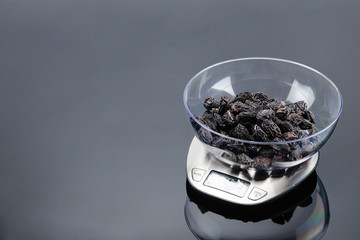 Dry plum in bowl on an electronic scale on grey mirror background with copy space