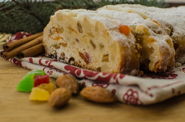 Christmas stollen on darkfestive background with fir twigs, lights and and berries. Close-up on this traditional German dessert