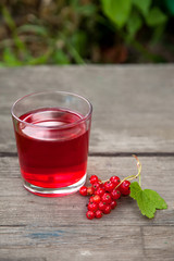 branch of red currant berries and a glass Cup with delicious berry juice on the edge of an old wooden table
