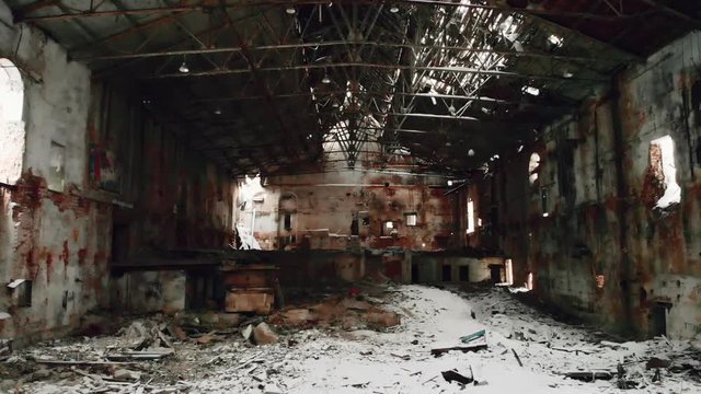 Flight on drone inside ruined factory or abandoned warehouse hall with broken roof and snow on floor, nuclear winter concept, toned