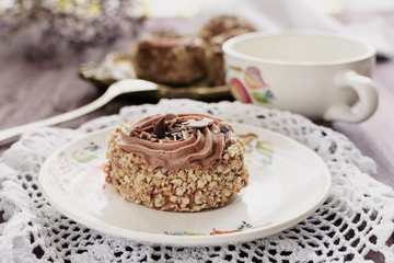 Biscuit cake sprinkled with nut crumb and decorated with chocolate cream on a white ceramic plate on a lacy dolly