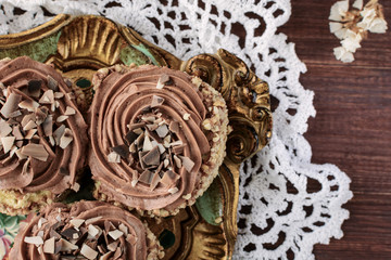 Biscuit cakes sprinkled with nut crumb and decorated with chocolate cream are on a vintage wooden tray on a white lace doily