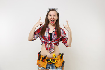 Strong excited handyman woman in plaid top shirt, denim shorts, kit tools belt full of instruments in protective goggles isolated on white background. Female in male work. Copy space for advertisement