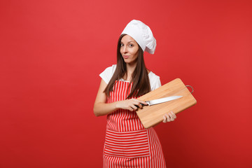 Housewife female chef cook or baker in striped apron, white t-shirt, toque chefs hat isolated on red wall background. Housekeeper woman holding wooden cutting board, knife. Mock up copy space concept.