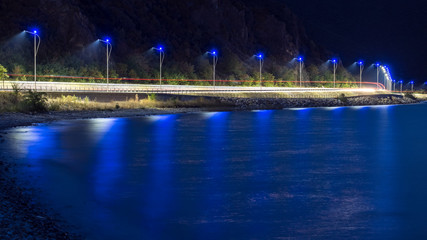 Car light trails and street lights along lake waterfront road at night