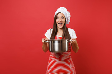 Housewife female chef cook or baker in striped apron white t-shirt toque chefs hat isolated on red wall background. Smiling surprised woman holding vacant crockery pot. Mock up copy space concept.