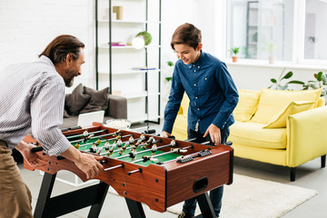 Happy teenager playing table football with his father at home