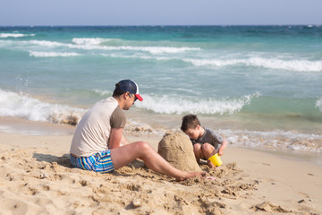 Fototapeta na wymiar Little kid boy and his father man building sandcastle on the beach. Summer vacation. Holidays.