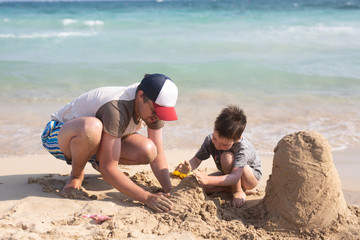 Young father and his little son building sand castle at beach