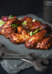 A beautiful platter slate plate full of organic delicious golden and crispy bbq chicken wings, served in a dark photography mechanic style environment. Surrounded by mechanic tools. food fashion.
