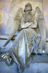 Genoa / Italy - June 20 / 2016 : Statue of a sitting old male angel with wings at monumental cemetery of Staglieno