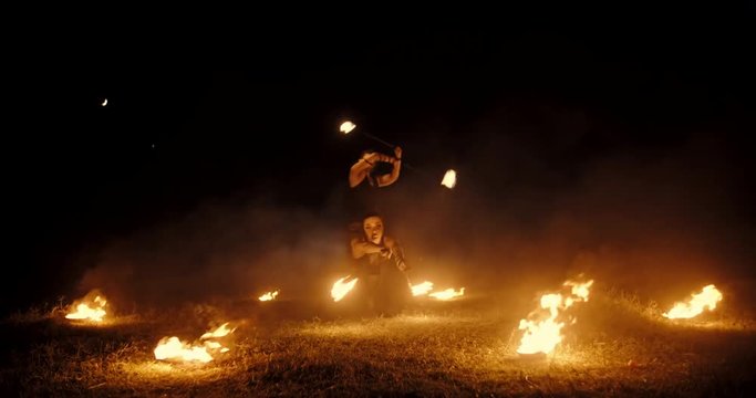 Coll fire show artists having a performance in the dark, swinging fire pieces between bowls with burning liquid - extreme slow motion
