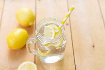Mason glass jar with water , fresh lemons and straws on wooden table. Summer. Hot. Fresh