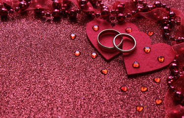  Red background with two rings and a heart, near small glass hearts and beads with a ribbon