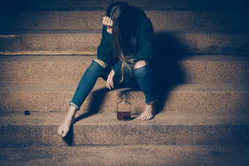 Young drunk woman sitting outside in night. Alcoholism and drug addiction lead to depression.