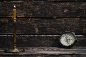 Compass and burning candle on the wooden table background with copy space. Travel or adventure concept.