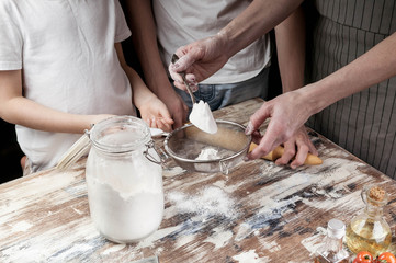 Mom with children sift flour for dough. Hands of mother and her children. Cooking with kids. Close-up