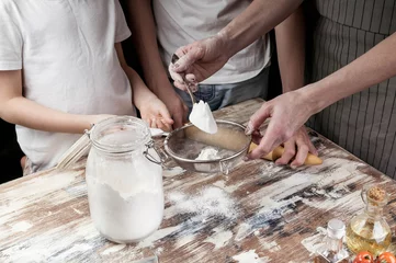 Foto op Canvas Mom with children sift flour for dough. Hands of mother and her children. Cooking with kids. Close-up © yusev