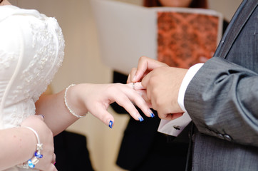 A wedding male groom is placing the wedding ring onto the brides finger. A promise to have each...