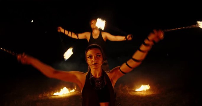 Coll fire show artists having a performance in the dark, swinging fire pieces between bowls with burning liquid - extreme slow motion