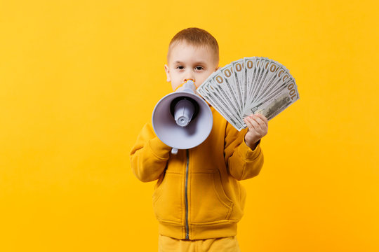 Little happy kid boy in yellow clothes hold fan of money in dollar banknotes, megaphone isolated on orange wall background, children studio portrait. Childhood lifestyle concept. Mock up copy space.