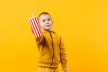 Fototapeta premium Little fun cheerful kid boy 3-4 years old wearing yellow clothes hold cup of soda isolated on orange wall background, children studio portrait. People, childhood lifestyle concept. Mock up copy space.