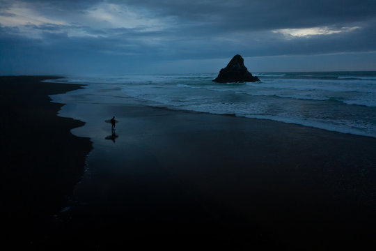 Silhouette of man with surfboard walking on beach