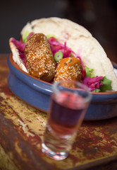 Beautiful lebanese falafel and salad in a pitta bread, served with spicy sauce, mayo and shots of alcohol spirits. Served in a ceramic bowl on a metal canister.